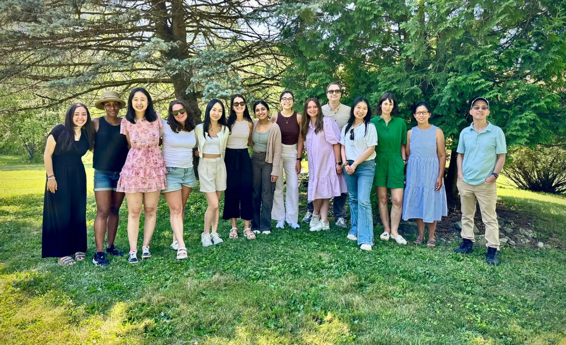 Members of the Stockwell Lab smile while standing in a grassy clearing in front of some trees.