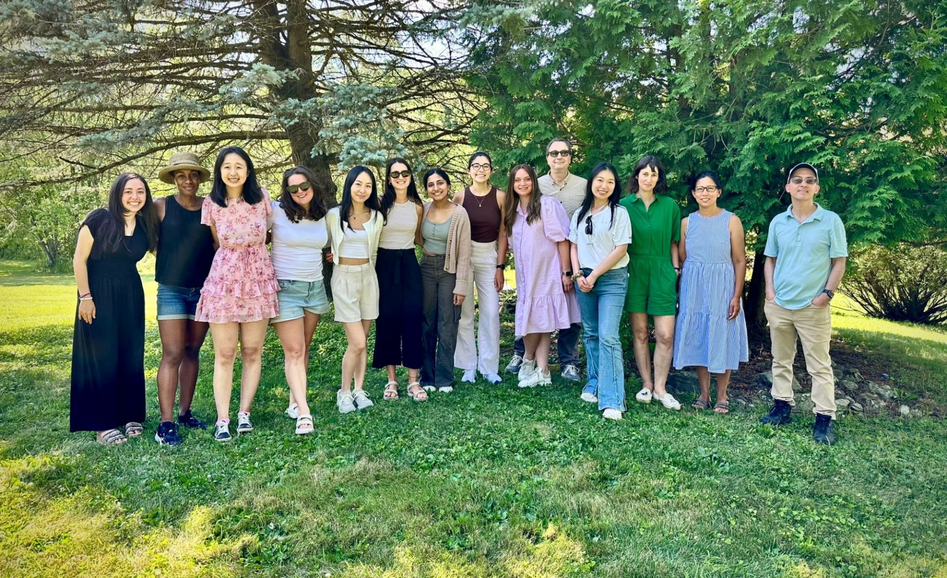 Members of the Stockwell Lab smile while standing in a grassy clearing in front of some trees.